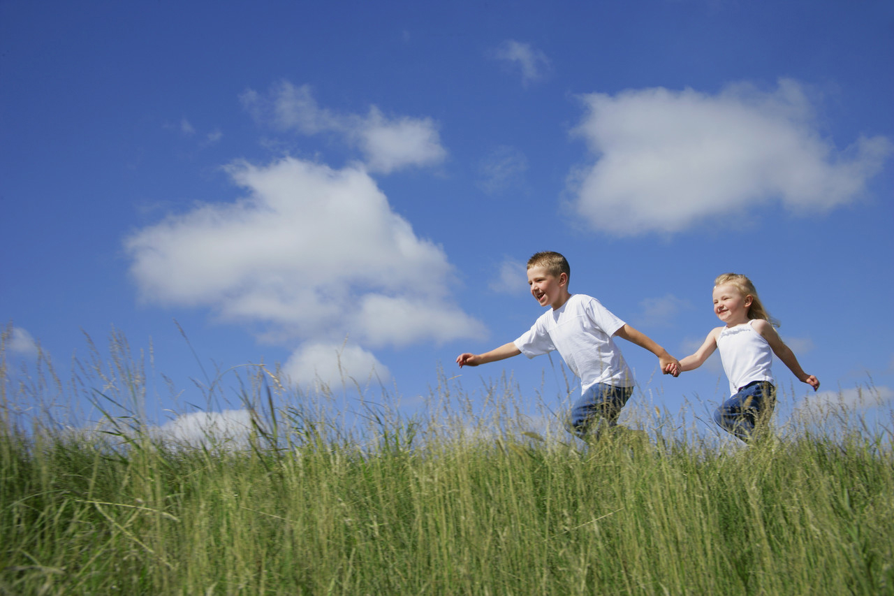 två barn som håller hand och springer över gräs
