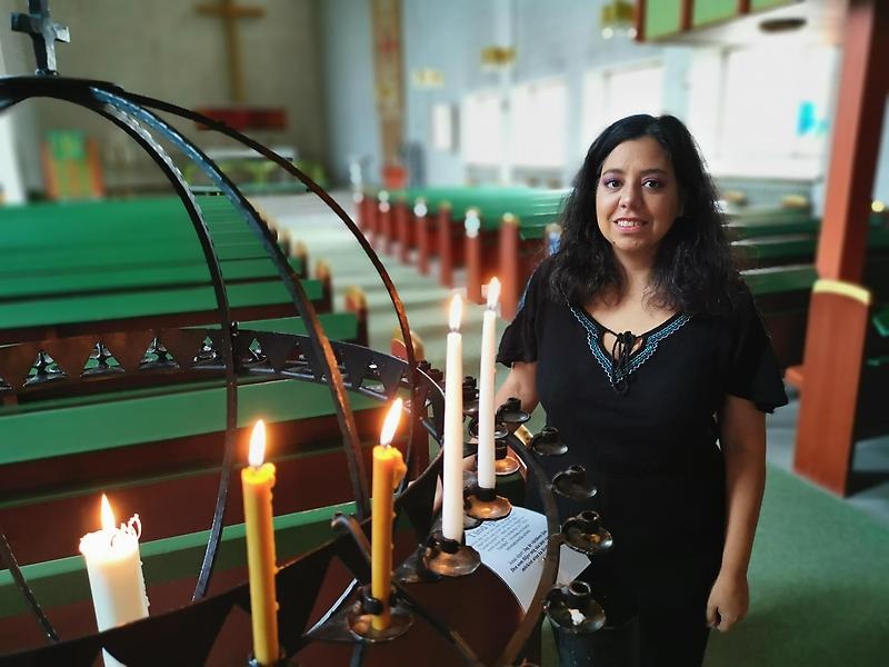 Kvinna står inne i kyrkan vid en ljusbärare med tända ljus